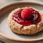 A beautifully styled cookie topped with a fresh raspberry on a neutral plate.